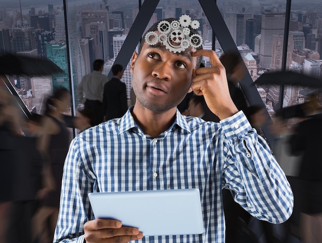 Young businessman thinking and holding tablet against room with large window looking on city