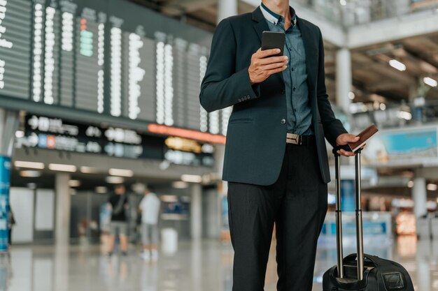 Young businessman at timetable screen board using smart phone.Flight board.