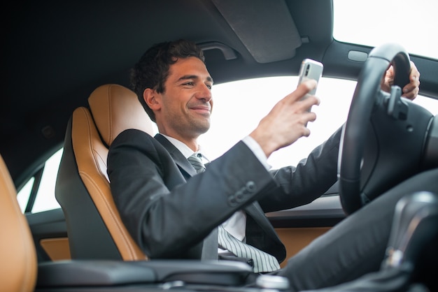 Young businessman using his mobile phone while driving, dangerous behaviour concept