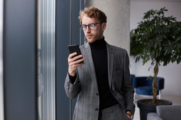 Young businessman using his smartphone planning meeting with colleagues in the office interior