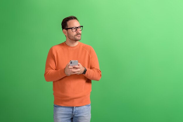 Foto giovane uomo d'affari che usa il cellulare e contempla mentre guarda lontano sullo sfondo verde