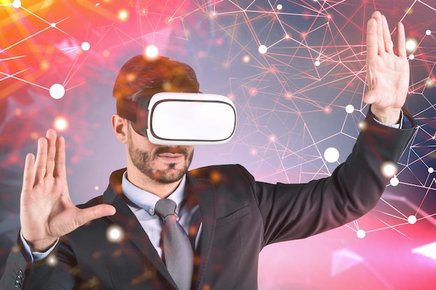 Young businessman in VR goggles and dark suit working and gesturing in virtual reality. Red network interface. Toned image