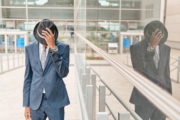 Young businessman wearing fashioned suit covering his face with his hat