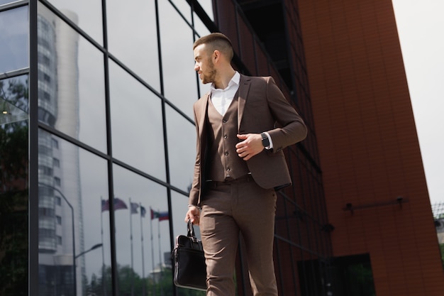 Young businessman with a briefcase running in a city street on a background of moder office building