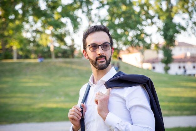 Photo young businessman with dark jacket over his shoulders and white shirt in a public garden