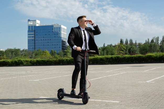 Молодой бизнесмен с электрическим скутером, стоящим перед зданием современного бизнеса