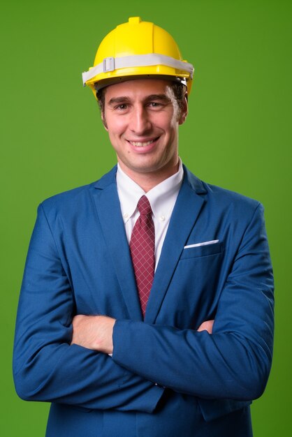 Young businessman with hardhat against green wall