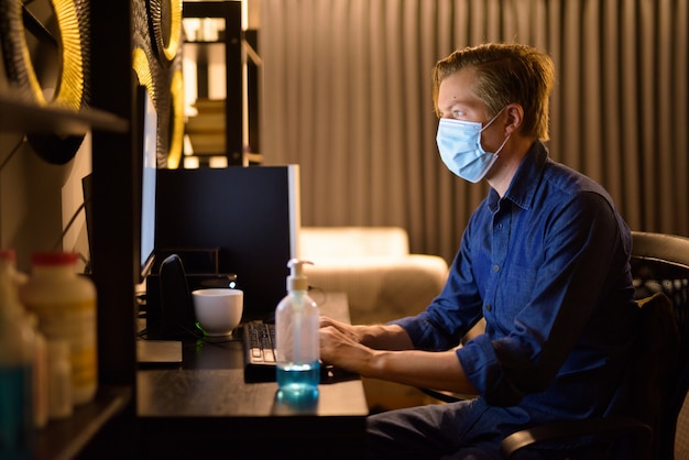 Young businessman with mask working from home late at night