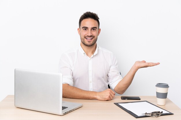 Young businessman with a mobile phone in a workplace extending hands to the side for inviting to come