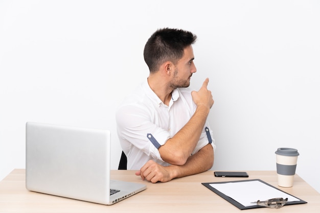 Young businessman with a mobile phone in a workplace pointing back with the index finger