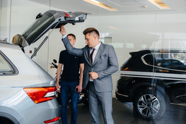 A young businessman with a salesman examines the trunk of a new car in a car dealership. Buying a car.