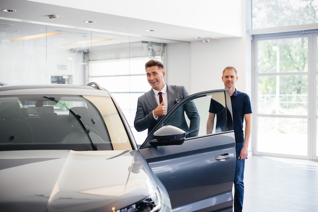 A young businessman with a salesman looks at a new car in a car dealership. Buying a car.