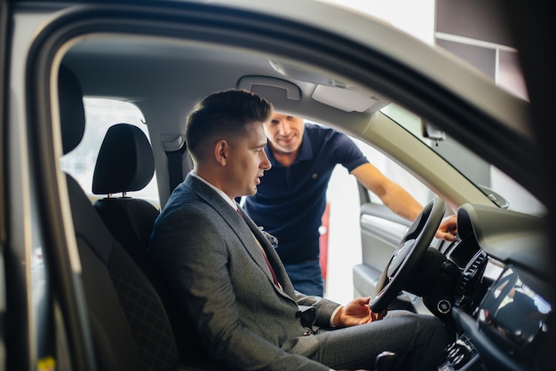 A young businessman with a salesman looks at a new car in a car dealership. Buying a car.