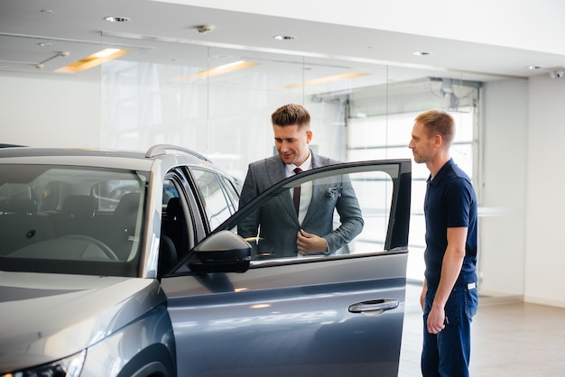 A young businessman with a salesman looks at a new car in a car dealership