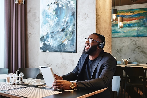 Young businessman with tablet pc and headphones sitting in cafe and networking