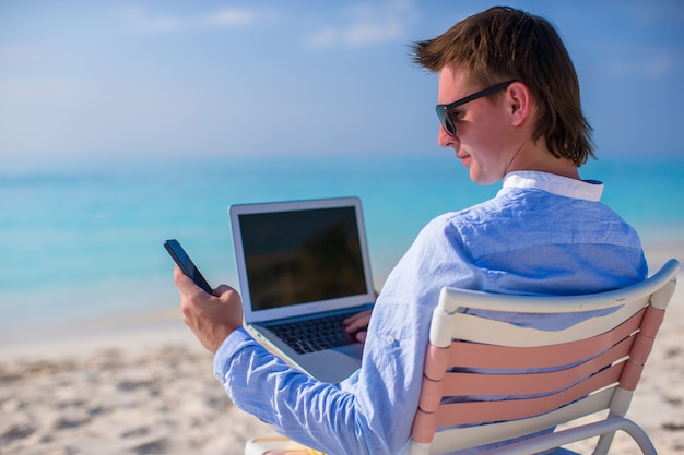 Young businessman working with laptop on tropical beach