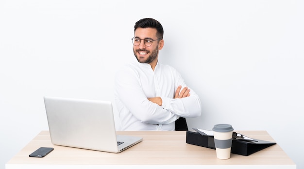 Young businessman in a workplace with arms crossed and happy