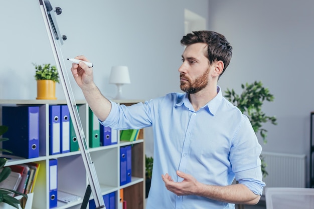 Young businessman writing on white board with marker business strategy plan man working in modern bright office