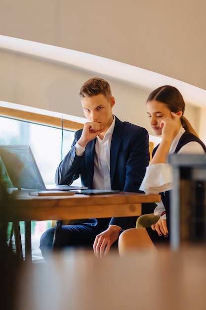 Young businessmen boy and girl work with a laptop, a tablet and notes in the cafe