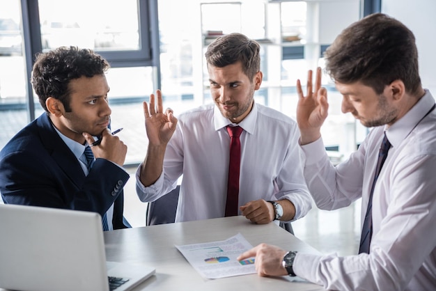 Young businessmen in formal wear discussing business charts and showing ok sign, business concept