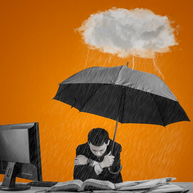 Young businessperson working in office while holding an umbrella