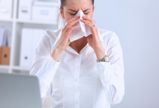 Young businesswoman blowing her nose sits at the desk