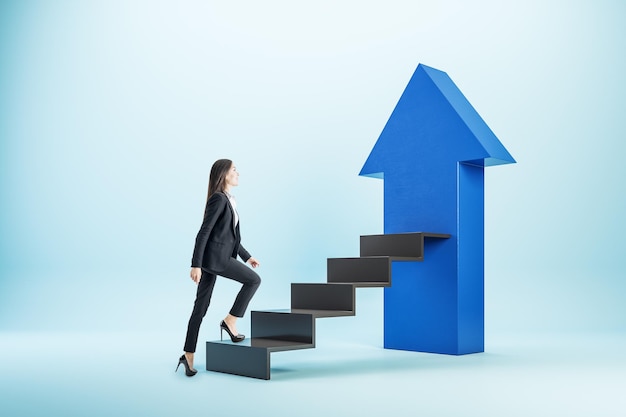 Молодая бизнесменка поднимается по черной лестнице с голубой стрелкой Концепция старта и успеха