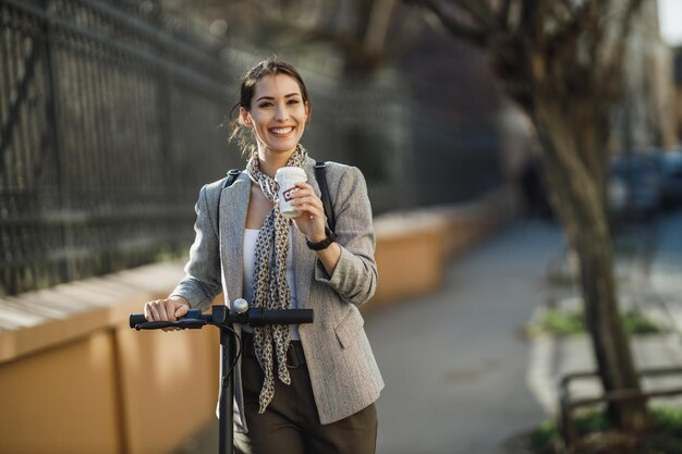 電動スクーターで仕事に行く間にコーヒーを飲む若い実業家。