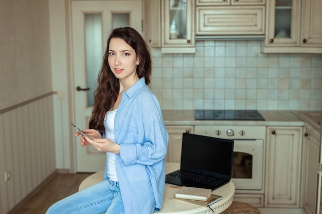 Photo young businesswoman girl in the home office in her kitchen works and conducts telephone conversations.