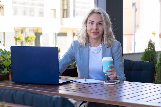 Giovane imprenditrice in abito grigio si siede a un tavolo in un bar e scrive note vedere il webinar.