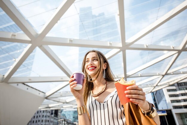 Giovane imprenditrice avente uno spuntino veloce con patatine fritte e caffè all'aperto vicino ai moderni uffici di brussel, belgio