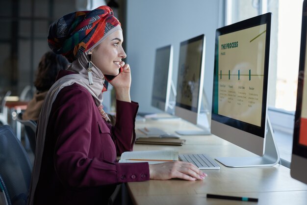 Young businesswoman in hijab looking at computer monitor and working over online presentation at office