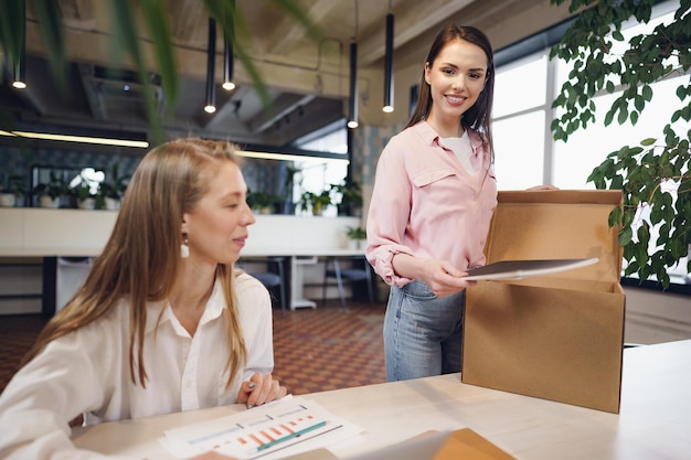 Young businesswoman holding box of personal belongings about to leave office after quitting job