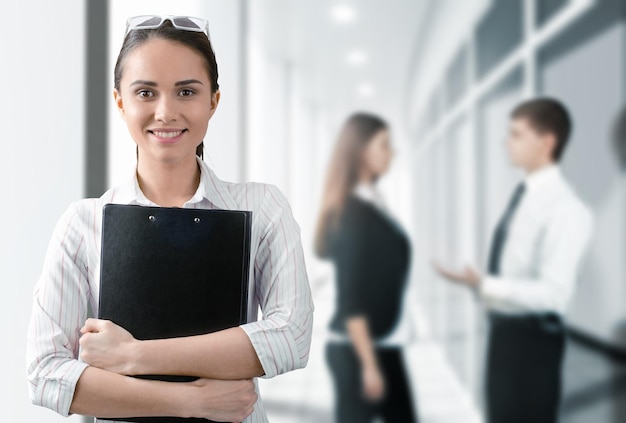 Young businesswoman holding folder, looking at camera on background