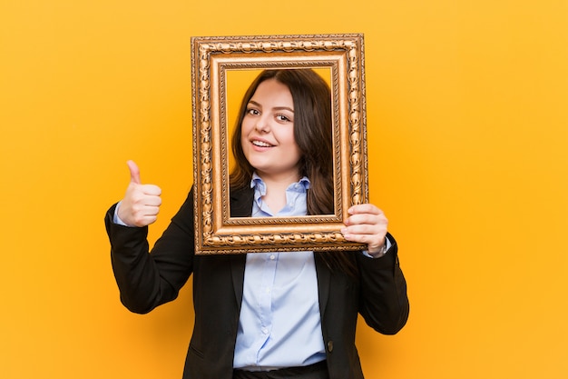 Young businesswoman holding a frame smiling and raising thumb up