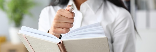 Young businesswoman holding notepad and ballpoint pen in office closeup