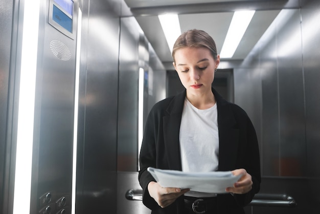 Young businesswoman is concentrated while reading the documents in the lift.