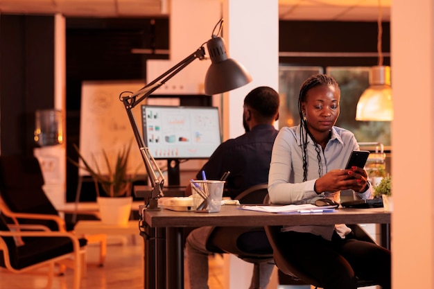 Young businesswoman looking at smartphone app to plan presentation, using social media website to create email report. Analyzing online data on mobile phone to do paperwork research.