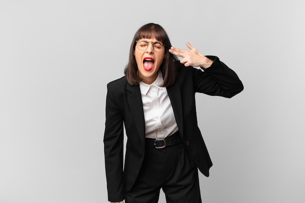 young businesswoman looking unhappy and stressed, suicide gesture making gun sign with hand, pointing to head