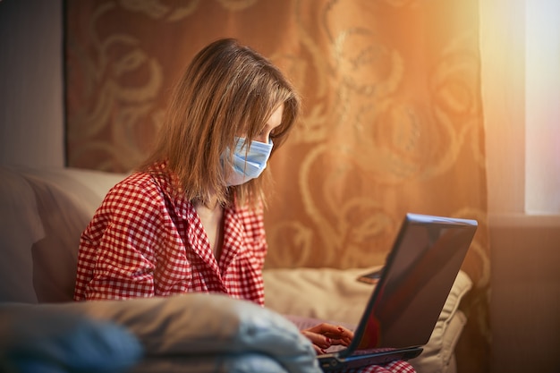 Photo young businesswoman in a medical protective mask works from home at the computer during self-isolation and quarantine. virus coronavirus outbreak, flu epidemic and covid ncov novel. stay home.