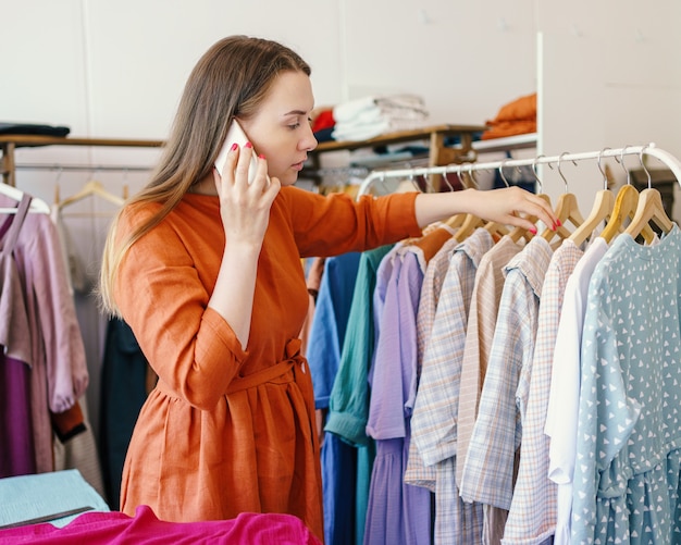 Young businesswoman owner of fashion atelier client on mobile phone and looking at dress collection