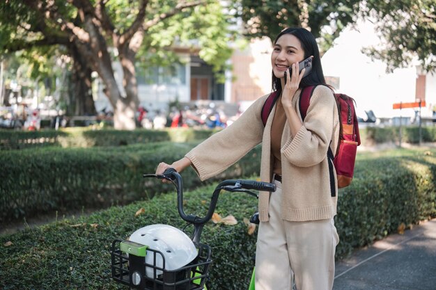 Foto giovane donna d'affari parcheggia la sua bicicletta e parla al telefono nel parco