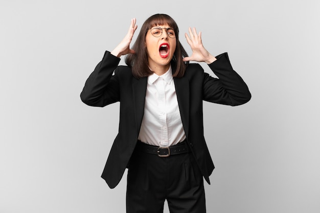 Young businesswoman screaming with hands up in the air, feeling furious, frustrated, stressed and upset