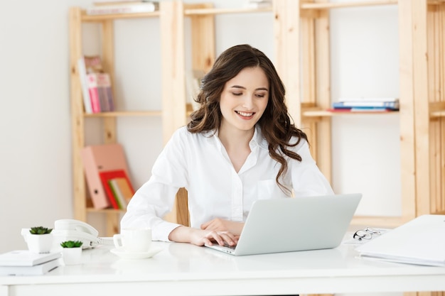 Young businesswoman or secretary sitting at desk and working Smiling and looking at camera