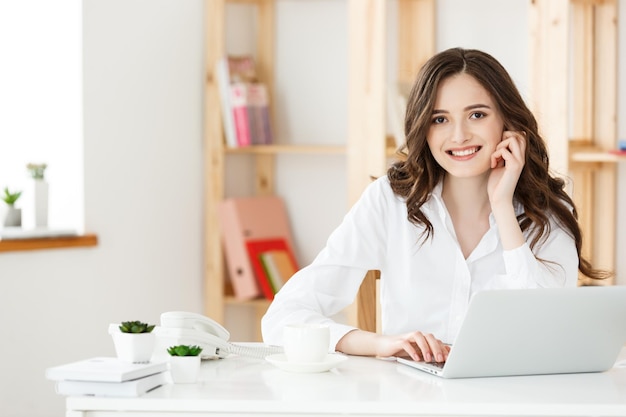 Young businesswoman or secretary sitting at desk and working Smiling and looking at camera