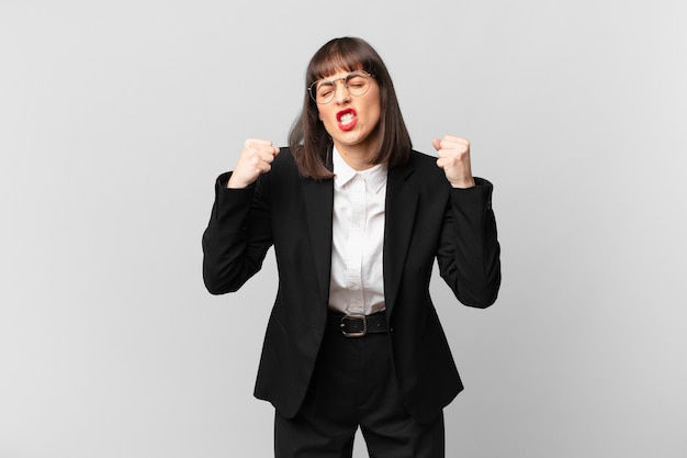 Young businesswoman shouting aggressively with an angry expression or with fists clenched celebrating success