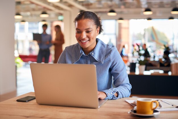 Young Businesswoman Sitting At Desk Working On Laptop In Modern Open Plan Office