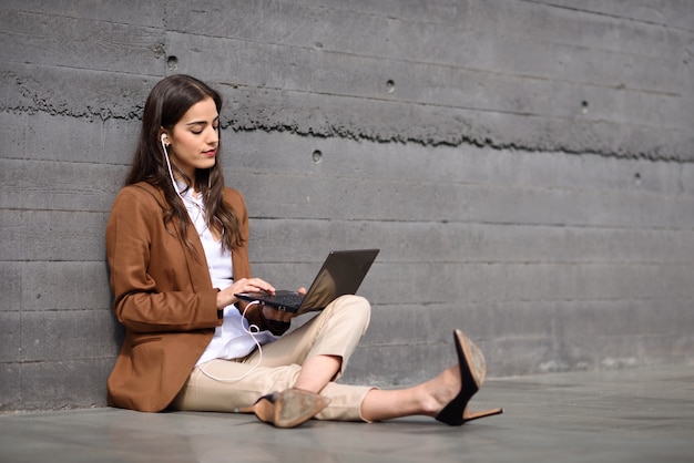 Giovane imprenditrice seduta sul pavimento a guardare il suo computer portatile. bella donna che indossa usura formale usando auricolari.