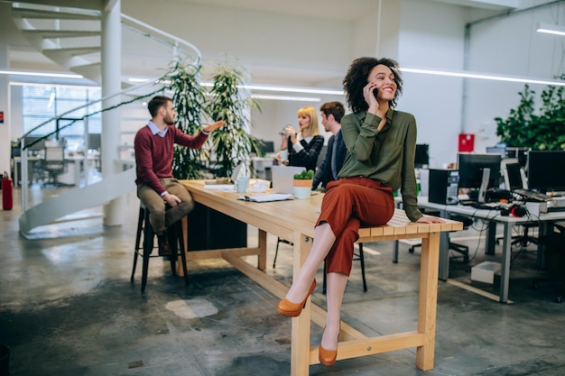 Young businesswoman sitting on the table, talking on the phone