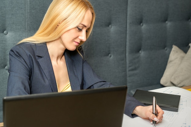 Young businesswoman sitting at the table and writing in a notebook. Adult woman working with papers at the cafe